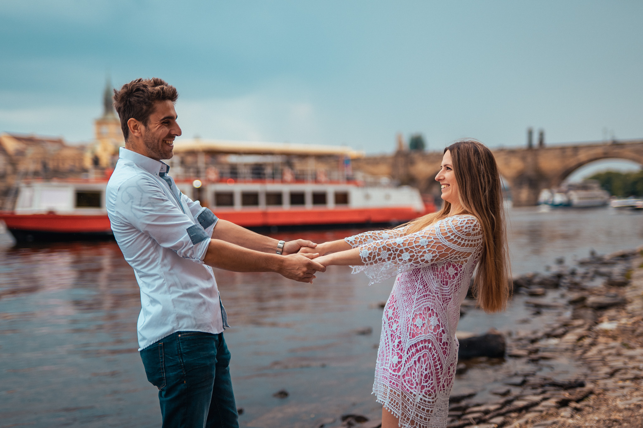 zamilovaný pár držící se za ruce u Karlova mostu s výhledem na projíždějící loď , Praha, 2023